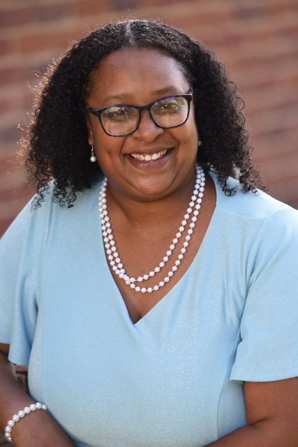 a photo of a young, friendly, smiling black woman wearing glasses and a pearl necklace